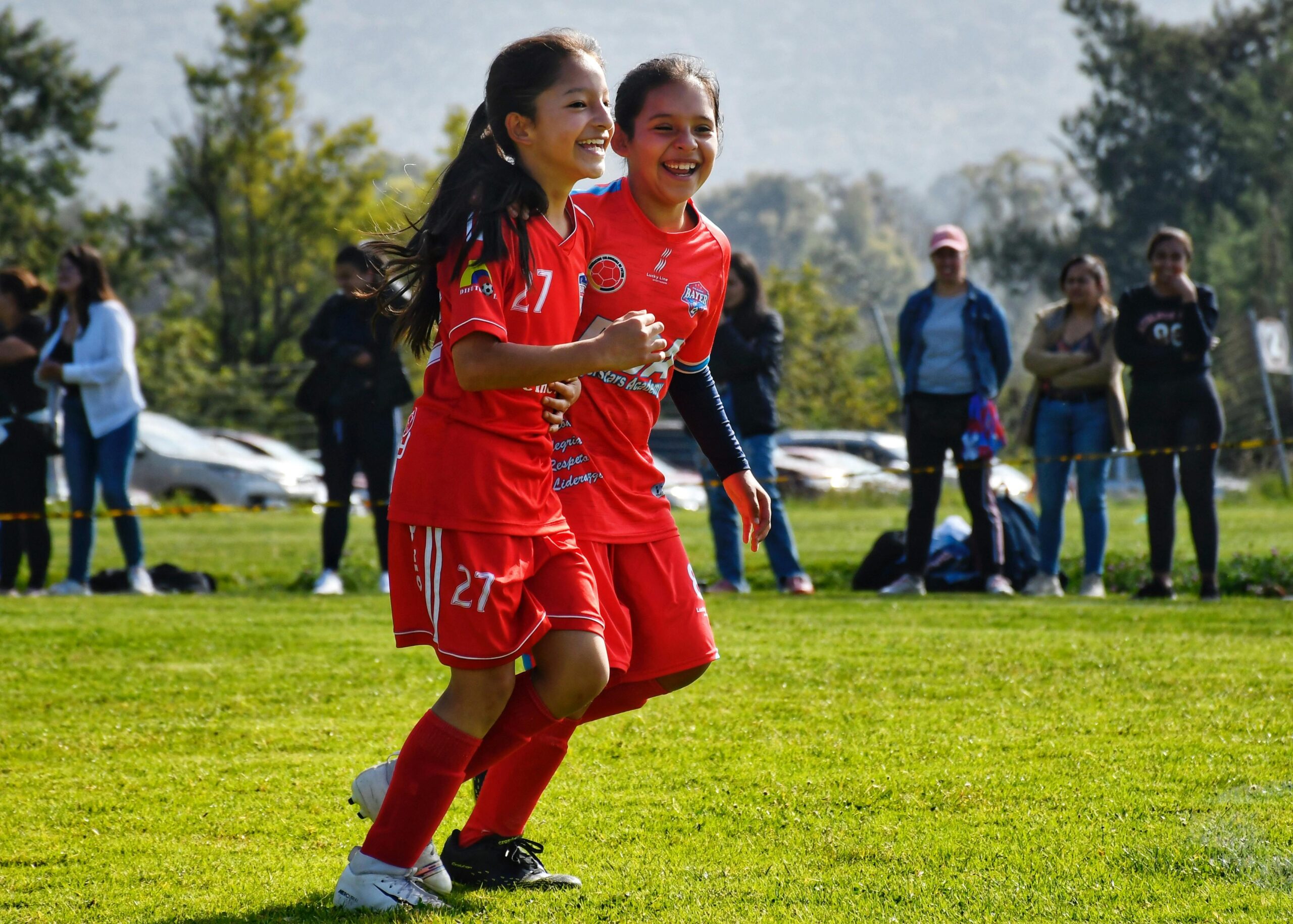 Two girls in red soccer uniforms having fun playing a youth match outdoors.